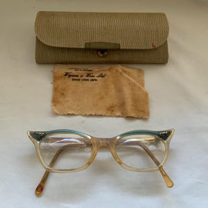 Op de afbeelding: Een vintage cat-eye bril met een lichtbruin montuur en teal blauwe accenten. De bril zit in een etui met een reinigingsdoekje waarop staat "Wyman & Sons Ltd.  Kingston,  Ontario,  Canada."