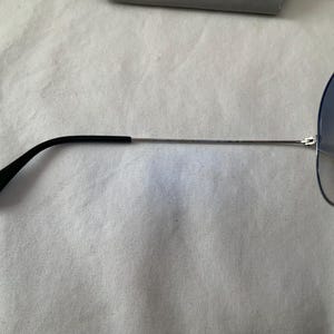May include: Aviator-style sunglasses with a silver frame and gradient blue lenses. The temples are black and extend to the ear. The sunglasses are partially visible against a white background.