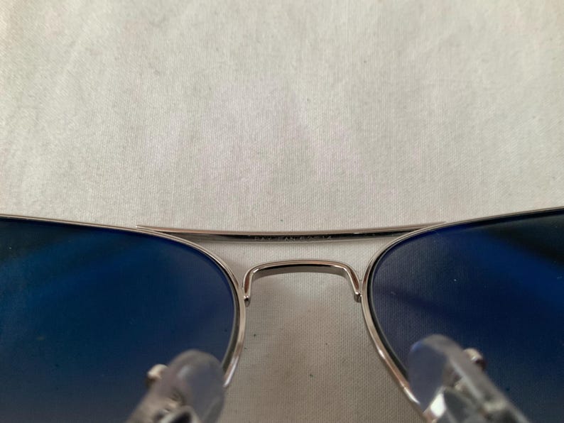 May include: Aviator-style sunglasses with a silver frame and gradient blue lenses. The top bar of the frame has the text "MADE IN FRANCE". The lenses are a deep blue color, and the frame has a classic, sleek design.