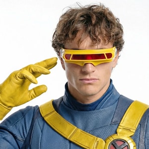 May include: A person wearing a blue and yellow costume with yellow gloves and a yellow visor with red lenses. The costume has a yellow strap across the chest and a circular emblem. The person is saluting.