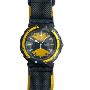 以下が含まれることがあります： 黒と黄色のSwatchの腕時計。黒いバンドと丸い文字盤。ベゼルは黒で、黄色の数字と黄色の秒針が付いている。