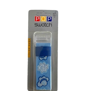 Może przedstawiać: Pasek do zegarka w niebiesko-białe wzory, z niebieskim paskiem i przezroczystą plastikową klamrą. Pasek jest zapakowany na kartce z nadrukiem "POP swatch".