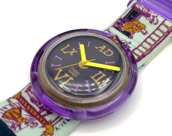 May include: A purple Swatch Pop watch with a black face and yellow hands. The watch has Roman numerals and the band is light green with a colorful design. The watch is a vintage accessory.
