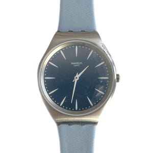 May include: A silver Swatch watch with a blue face and a light blue leather band. The watch face has white hands and hour markers.