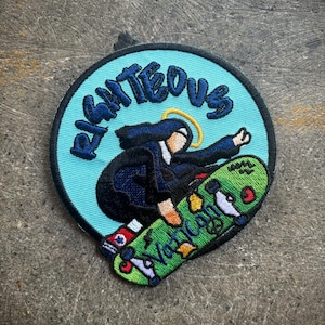 May include: Embroidered patch featuring a figure skateboarding, with the text "Righteous" in blue on a light blue circle. The skateboard is green with the text "Vatican" and other colorful details.