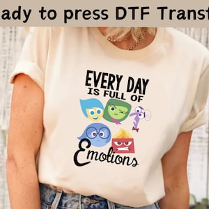 以下が含まれることがあります： インサイド・ヘッドのキャラクターが描かれた白いTシャツ。黒いグラフィックデザインで、「Every Day is Full of Emotions」というテキストが書かれています。