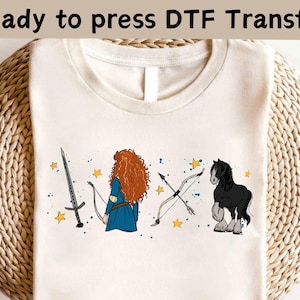 以下が含まれることがあります： クリーム色のTシャツ。剣、青いドレスを着たキャラクター、弓矢、黒い馬のデザイン。上部には「Ready to press DTF Transfer」の文字。