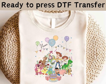 May include: Cream-colored t-shirt featuring a colorful graphic of cartoon characters, balloons, and a birthday cake. The text "Ready to press DTF Transfer" is at the top. The design includes the number 5 and the word "Name".
