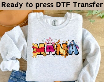 May include: A grey sweatshirt featuring a design of Winnie the Pooh and his friends spelling out "MAMA" in colourful letters. The design includes Tigger, Piglet, Eeyore, and Pooh Bear.