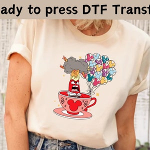 以下が含まれることがあります： クリーム色のTシャツ。映画「インサイド・ヘッド」のキャラクター、怒りの漫画のイメージがティーカップの中に入っています。ミッキーマウスの形をした風船と、上部に「Ready to press DTF Transfer」という文字が含まれています。
