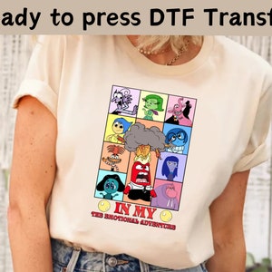 以下が含まれることがあります： 映画「インサイド・ヘッド」のキャラクターがプリントされた白いTシャツ。キャラクターは「In My Emotional Adventures」というテキストと共にグリッド状に配置されています。