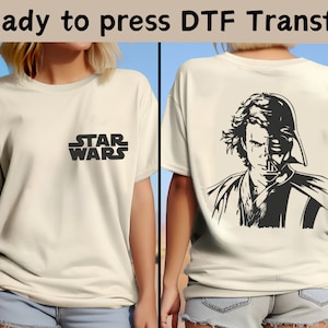 May include: A white t-shirt with a black "STAR WARS" logo on the front and a black and white illustration of Darth Vader and Anakin Skywalker on the back. The t-shirt is ready to be pressed with a DTF transfer.