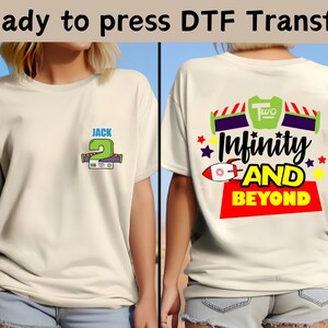 Puede incluir: Dos camisetas blancas con un diseño en la parte delantera y trasera. El diseño delantero es un número 2 verde con el nombre Jack encima. El diseño trasero es un cohete con el texto "Infinity and Beyond" y el número "Two" encima.