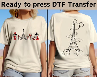 May include: A white t-shirt featuring a black and white design of Mickey Mouse and Minnie Mouse in front of the Eiffel Tower with the word "PARIS" printed below. The back of the shirt has a black and white design of the Eiffel Tower with Mickey Mouse ears on top.