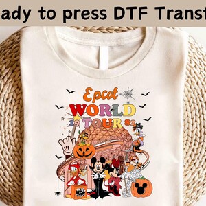 May include: Cream-colored t-shirt with a colorful graphic featuring the text "Epcot WORLD TOUR 82". The design includes cartoon characters, a pumpkin, and a stylized depiction of a theme park. The words "Ready to press DTF Transfer" are at the top.