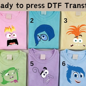 以下が含まれることがあります： 映画「インサイド・ヘッド」のキャラクターがプリントされた、明るい色のTシャツ6枚。キャラクターは、怒り、悲しみ、喜び、嫌悪、恐怖、そしてビング・ボン。Tシャツは1から6まで番号が付けられています。