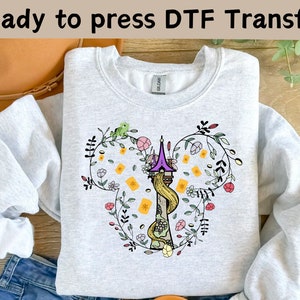 May include: A gray sweatshirt with a white design of a tower with a floral border. The tower is purple and yellow with a long braid of hair coming from the top. The design is in the shape of a Mickey Mouse head.
