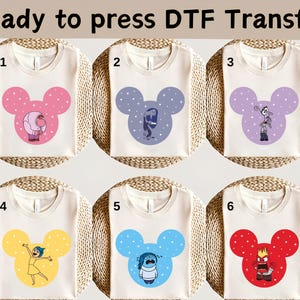 May include: Six cream-coloured t-shirts with different cartoon character designs. Each shirt features a Mickey Mouse-shaped design in various colours, including pink, blue, purple, yellow, and red. The text "Ready to press DTF Transfer" is at the top.
