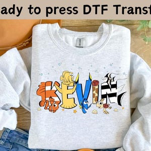 May include: A light gray sweatshirt with the name "KEVIN" in colorful cartoon lettering. The letters are decorated with characters from the movie "Finding Nemo". The text "Ready to press DTF Transfer" is at the top.