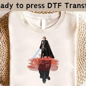 May include: Cream-colored t-shirt featuring a graphic of a character with a blue lightsaber, with a reflection of a dark figure. The text "Ready to press DTF Transfer" is at the top. The design is centered on the shirt.