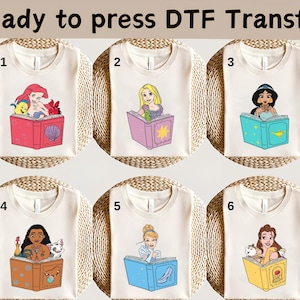 May include: Six cream-colored t-shirts with DTF transfers featuring Disney princesses reading books. The princesses include Ariel, Rapunzel, Jasmine, Moana, Cinderella, and Belle. The text "Ready to press DTF Transfer" is at the top.