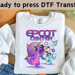 May include: A gray sweatshirt with a purple and blue graphic design featuring Mickey Mouse and a purple dragon. The graphic includes the text "EPCOT CENTER" in a gradient font.