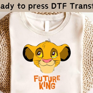May include: A white t-shirt with a cartoon image of Simba from The Lion King. The image is in orange, yellow, and brown. The text "FUTURE KING" is printed below the image in orange.