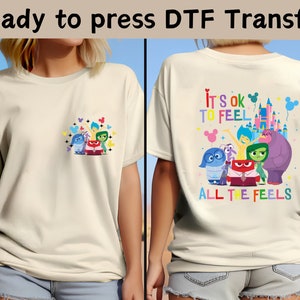 以下が含まれることがあります： インサイド・ヘッドのキャラクターがデザインされた白いTシャツ。デザインには、喜び、悲しみ、怒り、恐怖、嫌悪のキャラクターが含まれています。「すべての感情を感じることは大丈夫」というテキストがシャツに印刷されています。シャツは熱プレスでプレスする準備ができています。