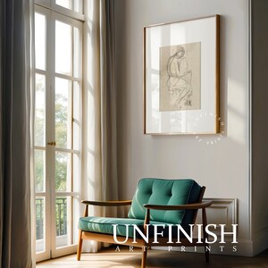 May include: A green armchair with wooden arms and legs sits in a room with a large window and a framed black and white drawing of a person on the wall. The text "UNFINISH ART PRINTS" is on the floor in front of the chair.