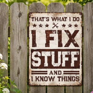 May include: A rectangular metal sign with a distressed, weathered finish. The text reads: THAT'S WHAT I DO, I FIX STUFF, AND I KNOW THINGS. It features a graphic of crossed screwdrivers and stars in dark brown ink against a cream-colored background.
