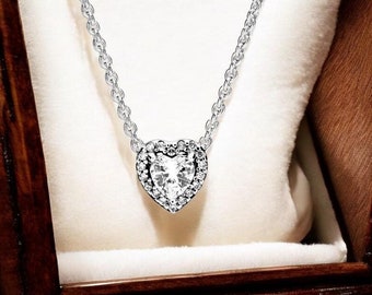 May include: A silver-toned necklace featuring a heart-shaped pendant with a central clear stone surrounded by a halo of smaller clear stones. The pendant hangs from a delicate silver-toned chain. The text BoujeexSociety is visible at the bottom.