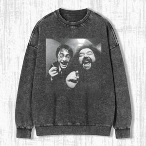 Könnte beinhalten: Ein anthrazitfarbenes Sweatshirt mit einem Schwarz-Weiß-Bild von zwei lachenden Personen. Das Bild befindet sich auf der Vorderseite des Sweatshirts. Das Sweatshirt hat einen Rundhalsausschnitt und lange Ärmel.
