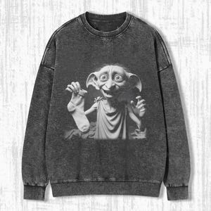 May include: A black and white graphic of Dobby from Harry Potter holding a sock is printed on a gray acid wash sweatshirt. The sweatshirt has a crew neck and long sleeves.