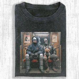 Puede incluir: Camiseta gris oscuro con un gráfico de Robocop y el Terminator en un vagón de metro, con un perro pequeño. La imagen tiene un aspecto vintage y desgastado. El Terminator lleva una chaqueta de cuero. La camiseta tiene cuello redondo.