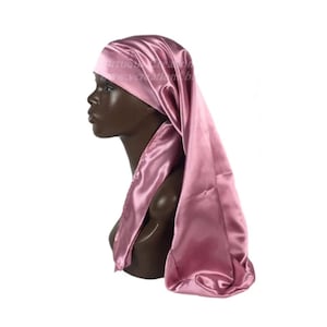 May include: A pink satin bonnet with a long tail. The bonnet is worn on a mannequin head.