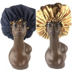 May include: Two satin bonnets, one gold and one navy blue, on mannequin heads. The bonnets are made of smooth, shiny fabric and have a gathered, ruffled edge.