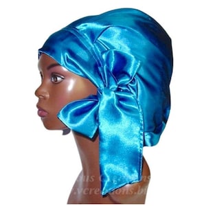 May include: A turquoise satin bonnet with a large bow on the side. The bonnet is designed to cover the head and protect hair. The satin material has a shiny appearance. The bow adds a decorative element to the head covering.
