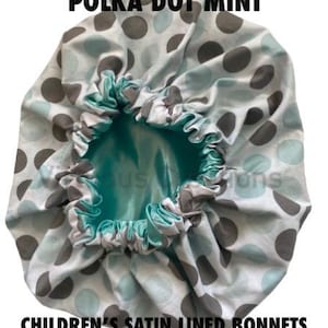 May include: A round bonnet featuring a white fabric exterior with a pattern of grey and light blue polka dots. The interior is lined with a solid, shiny turquoise satin fabric. The text POLKA DOT MINT and CHILDREN'S SATIN LINED BONNETS BY VIRTUOUS CREATIONS is visible.