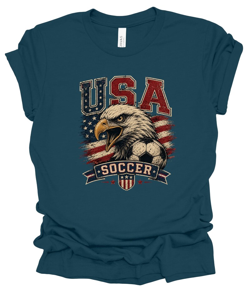 Peut inclure: Un t-shirt &agrave; manches courtes bleu sarcelle fonc&eacute; avec une impression graphique d'un pygargue &agrave; t&ecirc;te blanche, d'un ballon de football et du drapeau am&eacute;ricain. Le texte USA est imprim&eacute; en rouge et bleu au-dessus de l'aigle et SOCCER sur une banni&egrave;re.