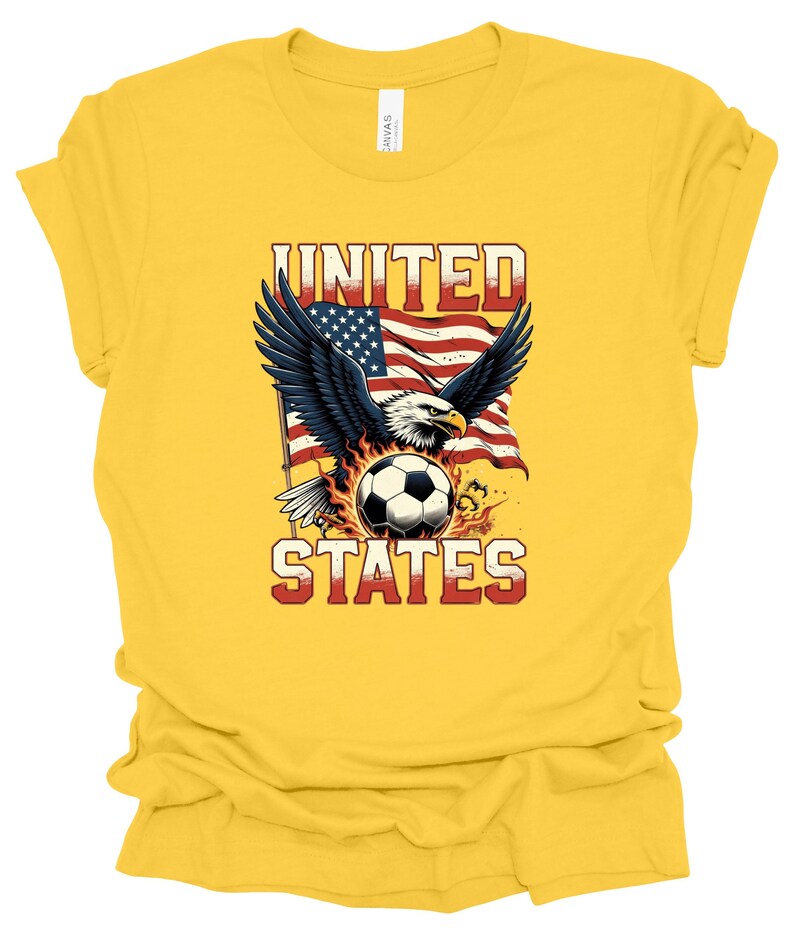 Op de afbeelding: Een felgeel T-shirt met korte mouwen en een afbeelding van een Amerikaanse zeearend met gespreide vleugels boven een voetbal, tegen een wapperende Amerikaanse vlag. De tekst UNITED staat boven de adelaar en STATES onder de bal.