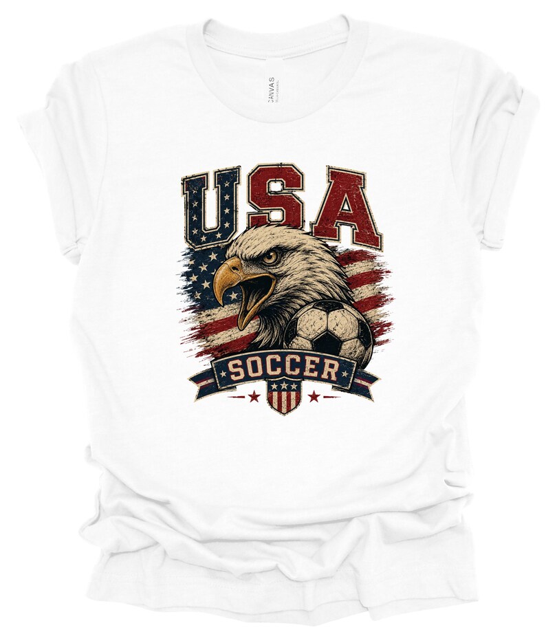 Peut inclure: Un t-shirt blanc &agrave; manches courtes avec une impression graphique repr&eacute;sentant un pygargue &agrave; t&ecirc;te blanche, un ballon de football et le drapeau am&eacute;ricain. Le texte USA est imprim&eacute; en grandes lettres au-dessus de l'aigle et SOCCER sur une banni&egrave;re.
