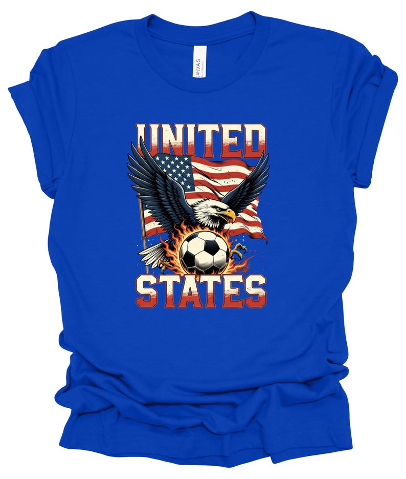 Op de afbeelding: Een koningsblauw t-shirt met korte mouwen en een grafische print van een Amerikaanse zeearend met gespreide vleugels boven een voetbal omringd door vlammen. Achter de adelaar wappert een Amerikaanse vlag. De tekst UNITED staat boven en STATES onder.