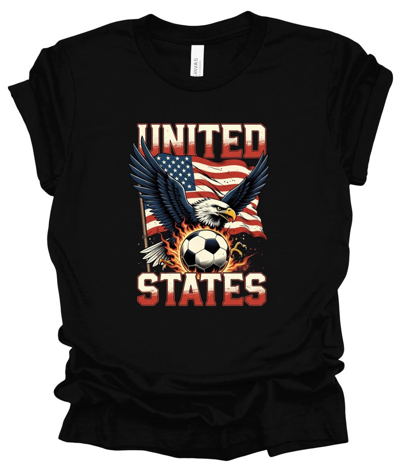 Op de afbeelding: Een zwart t-shirt met een afbeelding van een Amerikaanse zeearend met gespreide vleugels boven een voetbal omringd door vlammen. Achter de adelaar wappert een Amerikaanse vlag. De tekst UNITED en STATES is in het wit op het shirt gedrukt.