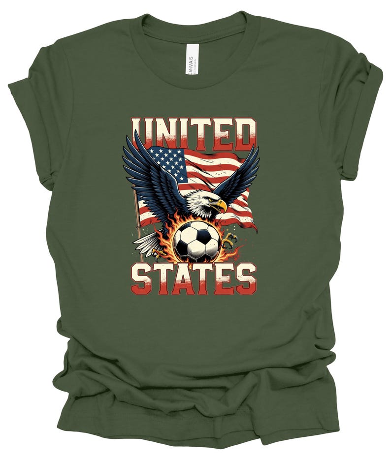 Op de afbeelding: Een olijfgroen t-shirt met een afbeelding van een Amerikaanse zeearend met gespreide vleugels boven een voetbal omringd door vlammen. Achter de adelaar is een Amerikaanse vlag te zien. De tekst UNITED staat boven de adelaar en STATES eronder.