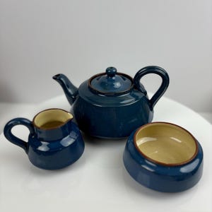 May include: A blue teapot, creamer and sugar bowl set. The teapot has a rounded body and a lid with a knob. The creamer and sugar bowl are both round and have a small handle.