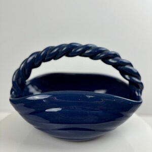 May include: A dark blue ceramic bowl with a twisted rope handle. The bowl has a wavy, organic shape.