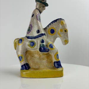 May include: A ceramic figurine of a person riding a horse. The person is wearing a hat and a colorful robe. The horse is white with blue and yellow polka dots.