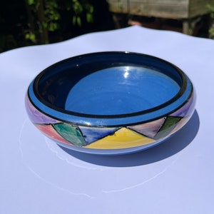 Könnte beinhalten: Eine blaue Keramikschüssel mit schwarzem Rand und einem farbenfrohen geometrischen Muster. Das Muster zeigt Dreiecke in den Farben Rosa, Gelb, Grün und Blau.