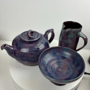 May include: A purple and green ceramic teapot, creamer, and bowl. The set has a swirl pattern and a glossy finish.