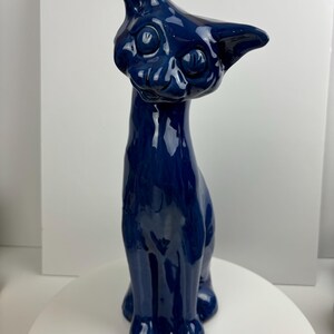 May include: A blue ceramic cat figurine with a whimsical expression. The cat is sitting upright with its tail curled around its body.